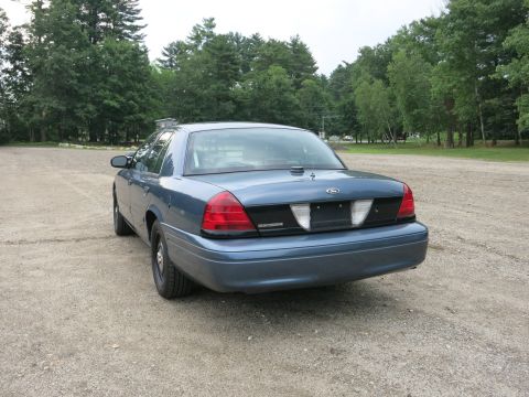 2001 Ford Crown Victoria - Rear view of a blue Ford Crown Victoria parked outdoors on a gravel surface with trees in the background.