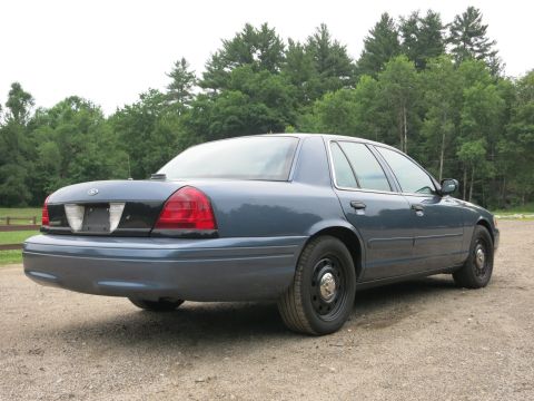 2001 Ford Crown Victoria - A blue 2001 Ford Crown Victoria sedan is parked on a gravel surface, with a wooded area behind it.