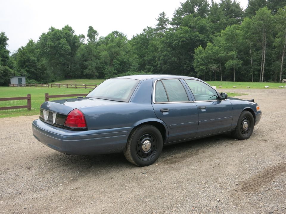 Blue 2001 Ford Crown Victoria parked on a gravel lot with trees in the background