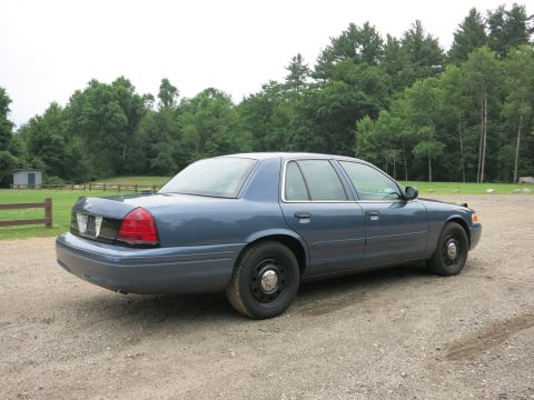 2001 Ford Crown Victoria - A blue 2001 Ford Crown Victoria is parked on a gravel surface with a wooded area behind it.