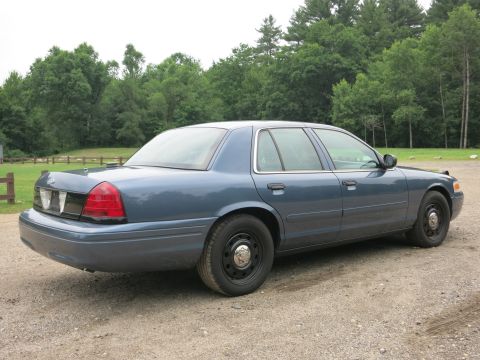 2001 Ford Crown Victoria - A blue 2001 Ford Crown Victoria is parked on a gravel surface with a wooded area behind it.