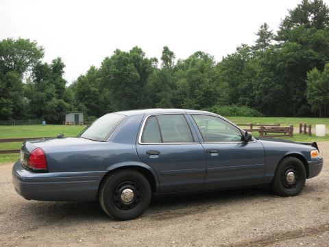 2001 Ford Crown Victoria - A blue 2001 Ford Crown Victoria sedan is parked on a gravel surface with a wooded area behind it.