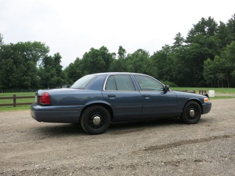 2001 Ford Crown Victoria - Side profile of a blue 2001 Ford Crown Victoria sedan parked outdoors on a gravel surface.