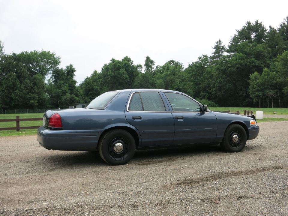 2001 Ford Crown Victoria sedan, side view, parked on gravel with trees in background