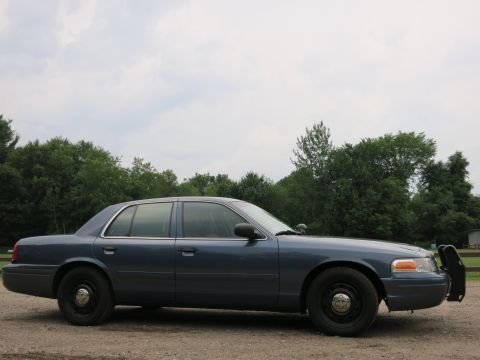 2001 Ford Crown Victoria - Side view of a blue 2001 Ford Crown Victoria police car parked outdoors with trees in the background.