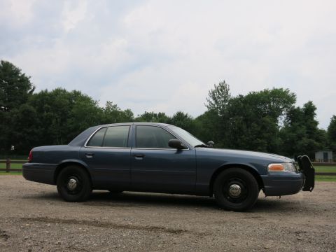 2001 Ford Crown Victoria - Side profile of a dark blue 2001 Ford Crown Victoria police car parked on a gravel lot.