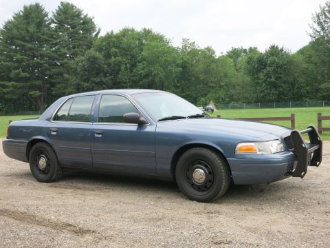 2001 Ford Crown Victoria - A blue 2001 Ford Crown Victoria sedan equipped with a push bar is parked outdoors.