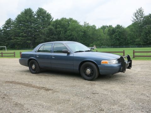 2001 Ford Crown Victoria - Blue 2001 Ford Crown Victoria police car with a push bumper is parked outside.