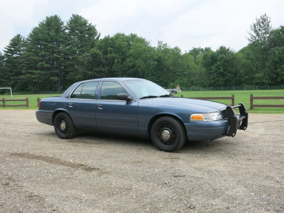 2001 Ford Crown Victoria police car, blue, with push bumper, parked on gravel lot