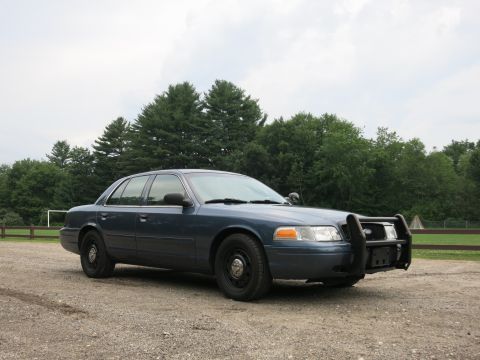 2001 Ford Crown Victoria - Blue 2001 Ford Crown Victoria police car with a push bumper is parked outside.