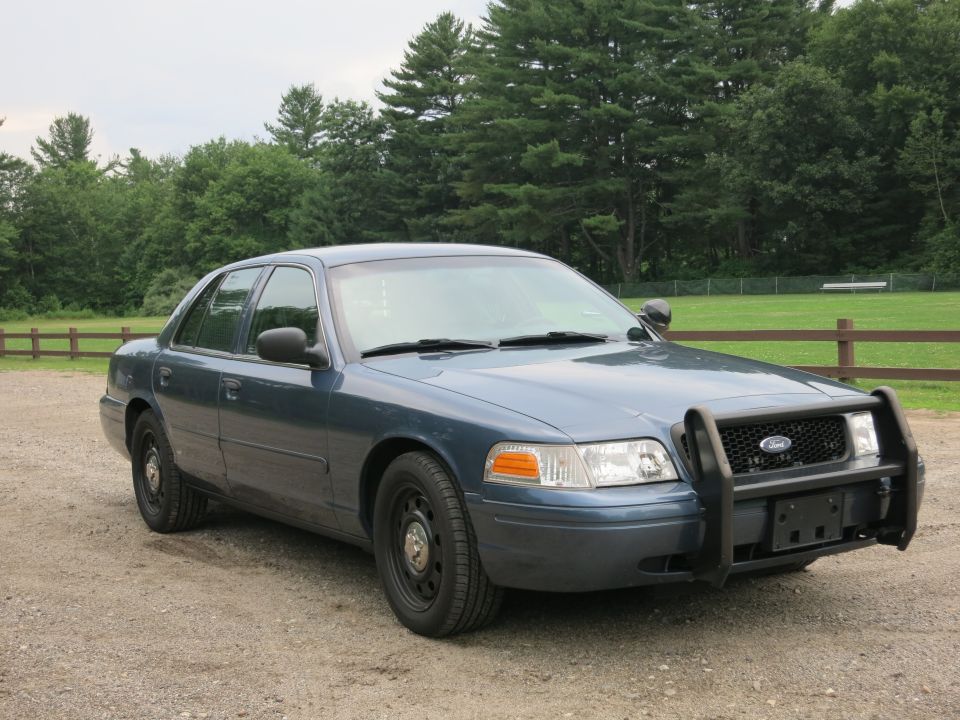 Blue 2001 Ford Crown Victoria with push bar, parked on gravel
