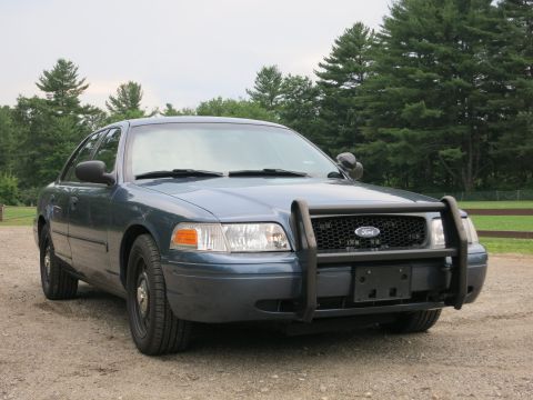 2001 Ford Crown Victoria - This Ford Crown Victoria police car is parked outdoors on a gravel surface, with a wooded area behind it.