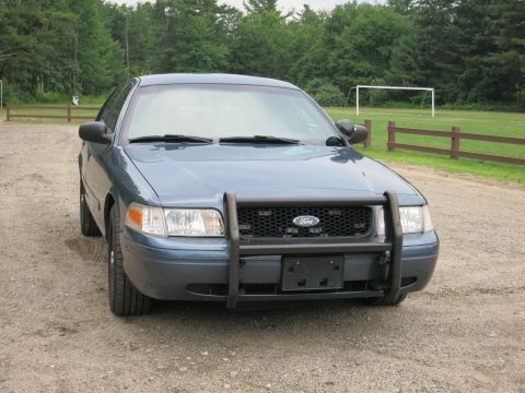 2001 Ford Crown Victoria - A blue Ford Crown Victoria with a push bar is parked on a gravel lot with a soccer goal in the background.