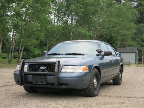 2001 Ford Crown Victoria - A blue 2001 Ford Crown Victoria police car equipped with a push bumper is parked outdoors.