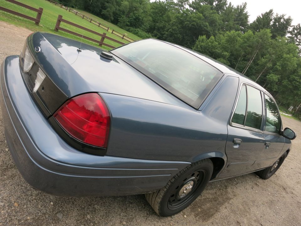 Rear three-quarter view of a blue 2001 Ford Crown Victoria parked on a dirt road