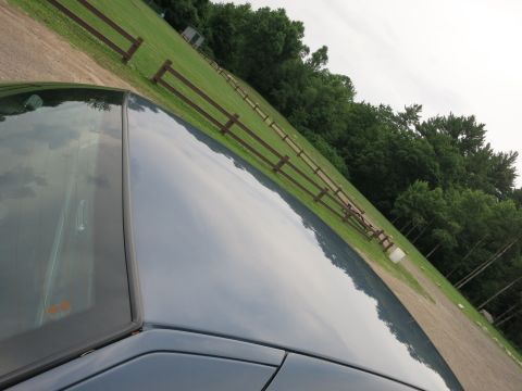 2001 Ford Crown Victoria - A car's roof and windshield are visible, reflecting the sky and a fence in a grassy area.