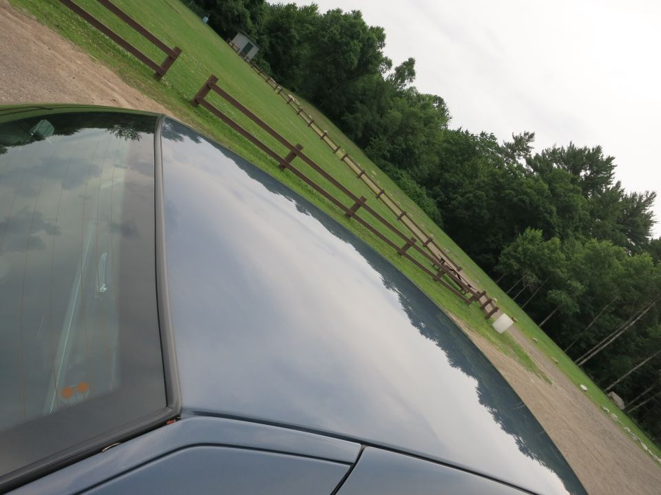 Dark blue car roof and windshield reflecting a cloudy sky and a wooden fence