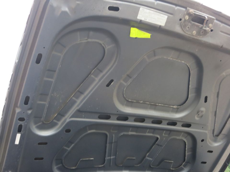 Underside of dark gray car hood with stamped bracing and two stickers