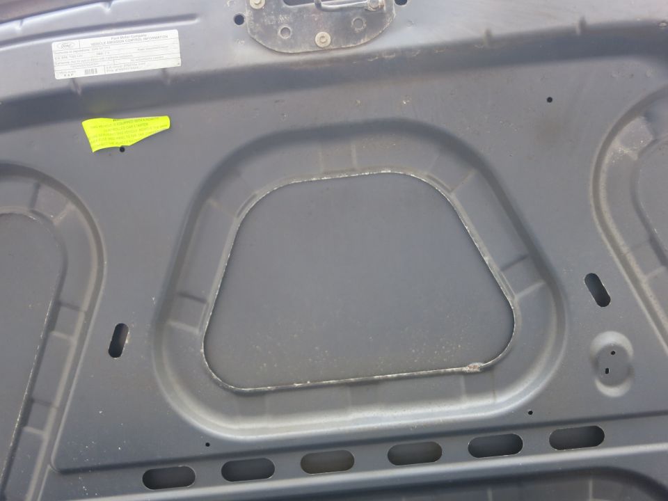 Underside of a gray car hood with a yellow sticker and a white label