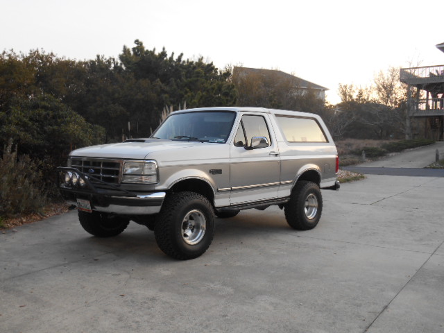 Two-tone silver and white Ford Bronco with aftermarket lights and large tires parked on a concrete driveway