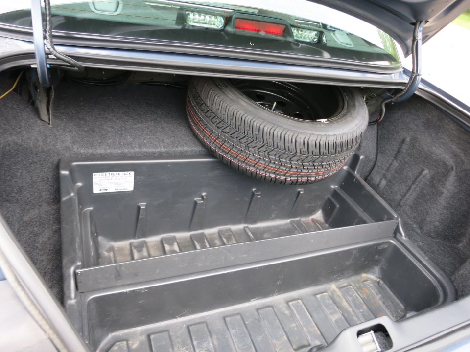 Trunk interior showing spare tire and plastic organizer tray. Label on tray reads 'POLICE TRUNK PACK'