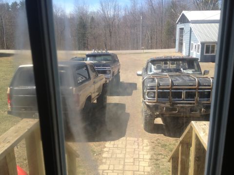 1970 Ford F-250 - Three trucks, including a black Ford F-250 and two Ford Broncos, are parked outside a blue building.