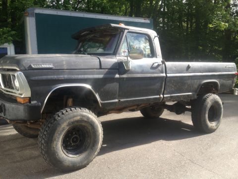 1970 Ford F-250 - This lifted Ford pickup truck is shown from the side, with a large trailer in the background.