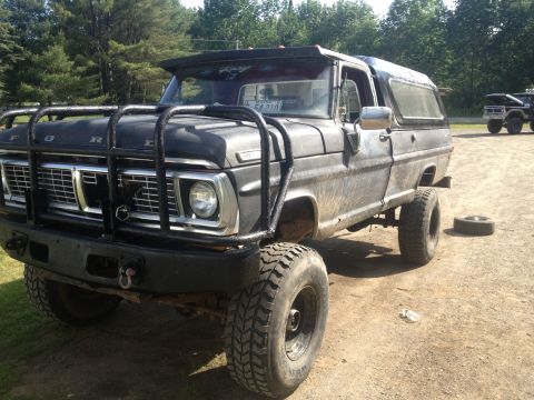 1970 Ford F-250 - This 1970 Ford F-250 features a heavy-duty brush guard and a camper shell, parked in a dirt lot.