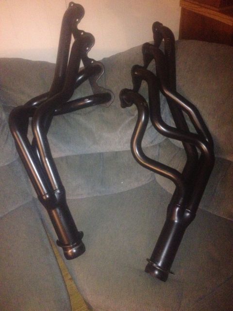 1970 Ford F-250 - Two black exhaust headers are displayed on a couch, with a SuperMotors.net watermark visible.