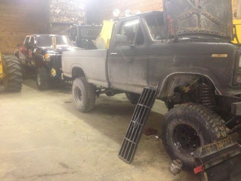 1970 Ford F-250 - Two pickup trucks are parked in a garage, one with its hood up and the other partially visible behind it.