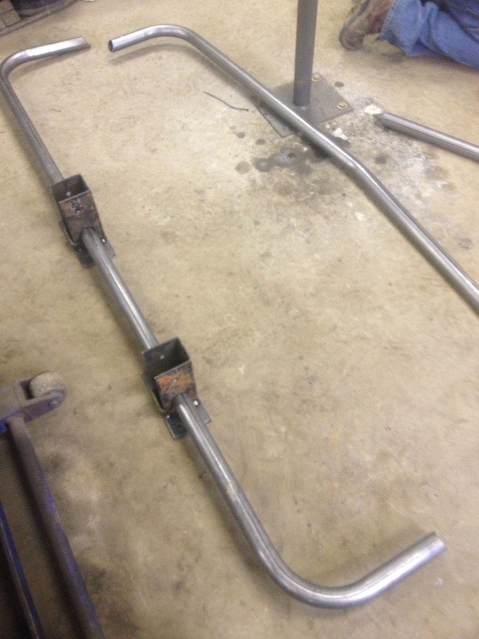 Metal tubing with square brackets welded on, lying on a concrete floor