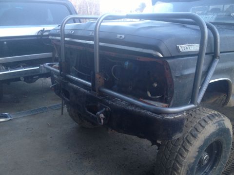 1970 Ford F-250 - A black 1970 Ford F-250 truck is shown with a custom front bumper and roll cage, with another vehicle partially visible to the left.