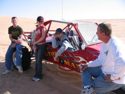 1993 Ford Taurus - A group of people relax around a red dune buggy in a sandy desert landscape.