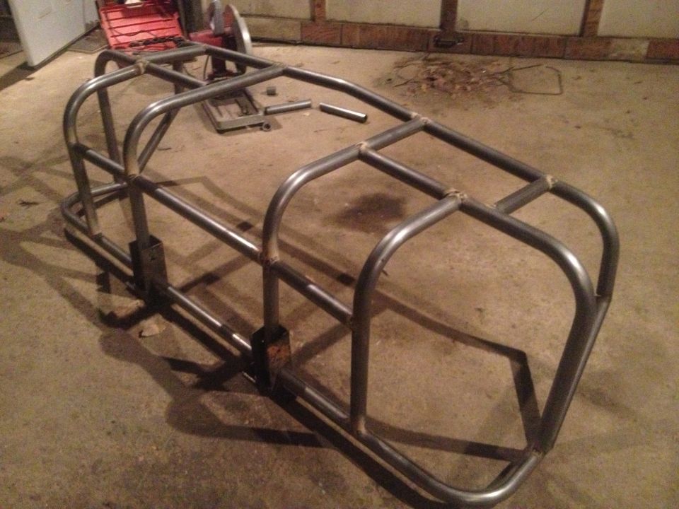 Bare metal custom roll cage frame with welded tubing, sitting on a concrete floor