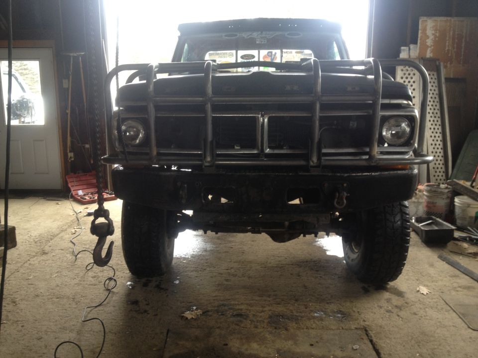 Black 1970 Ford F-250 with a large front brush guard, seen head-on in a garage