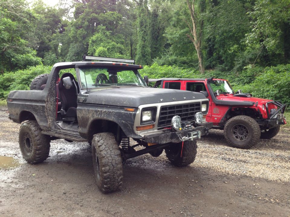 Black 1979 Ford Bronco with off-road modifications parked next to a red Jeep