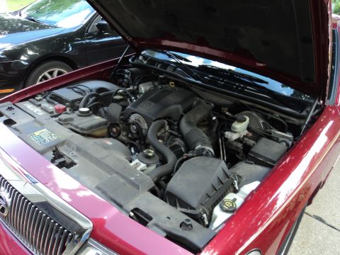 2004 Mercury Grand Marquis - The engine bay of a red 2004 Mercury Grand Marquis is shown with the hood open, parked next to a black car.
