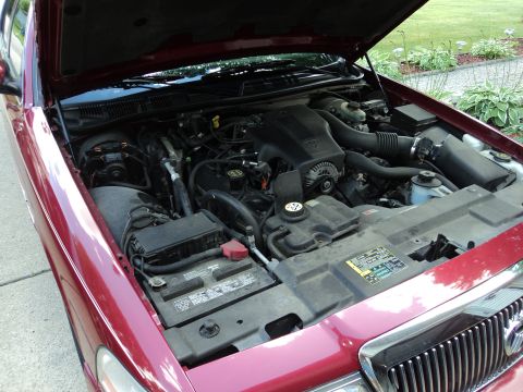 2004 Mercury Grand Marquis - Engine compartment of a maroon Mercury sedan with the hood raised, showing the V8, air box and battery in a driveway.