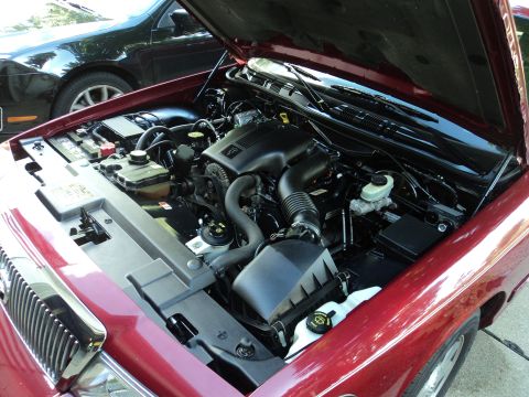 2004 Mercury Grand Marquis - Engine bay of a red 2004 Mercury Grand Marquis, with a black car visible in the background.