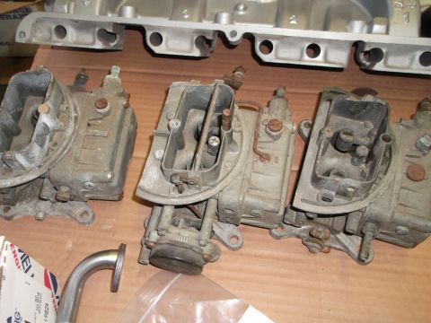1963 Ford Galaxie - A collection of vintage carburetors and an aluminum intake manifold are laid out on a wooden surface.