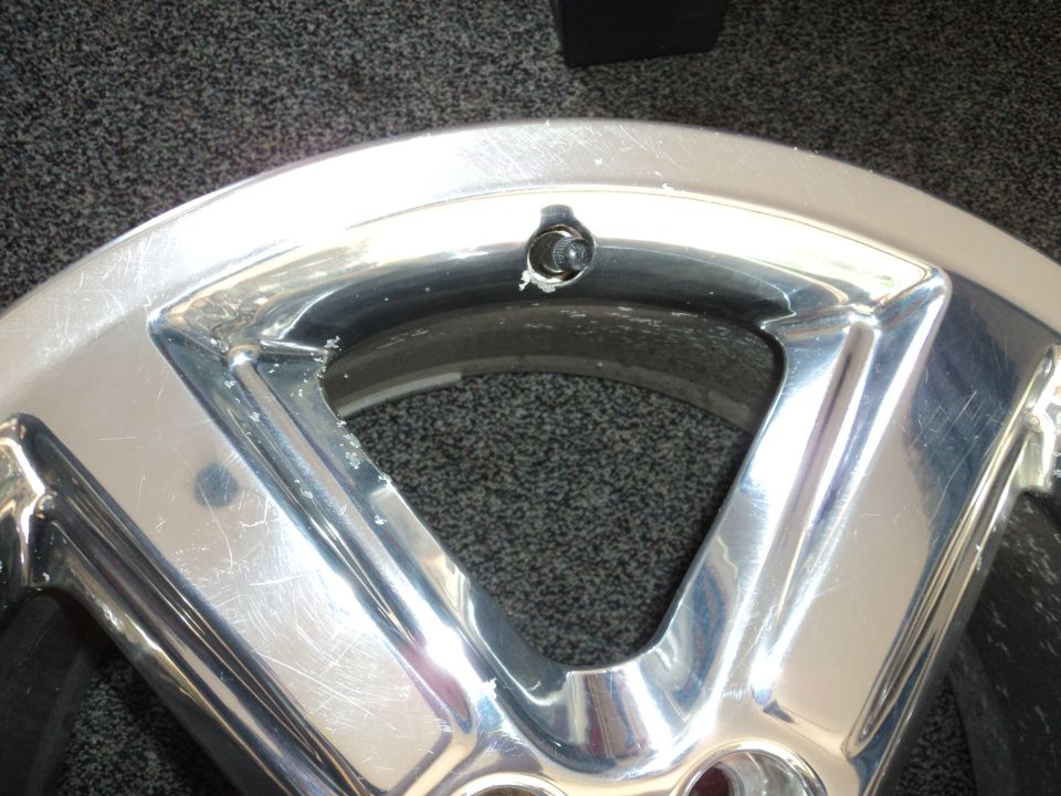 Chrome alloy wheel with visible damage near the valve stem opening
