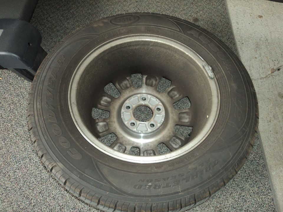 Wheel with a Goodyear tire, showing a silver rim with multiple lug nut holes and some dirt