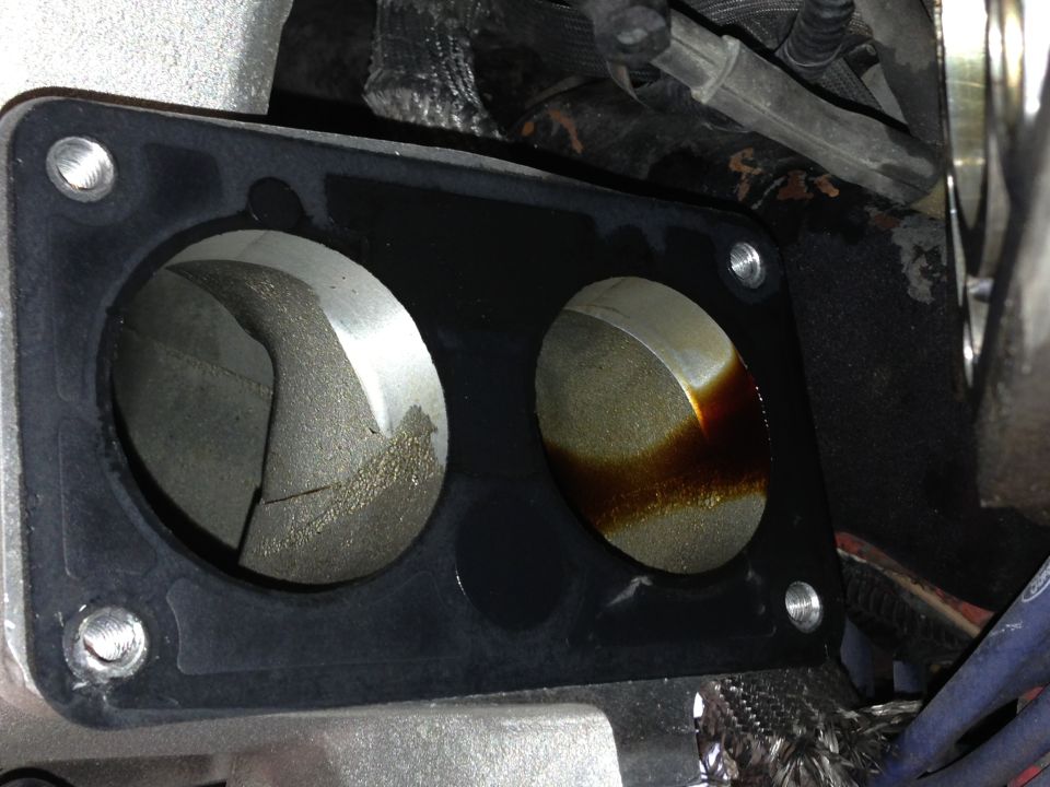 Engine intake manifold gasket with two openings, one showing internal damage and the other with oil residue