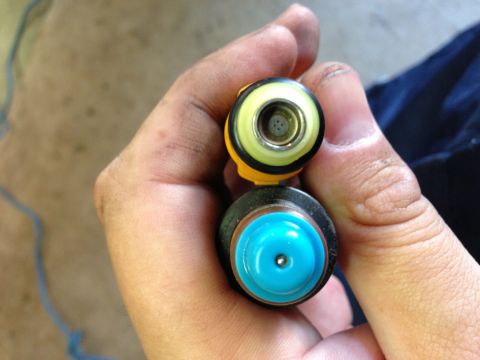 1989 Ford Bronco - A close-up view of two fuel injectors, one with a yellow top and the other with a blue top, being held by a person.