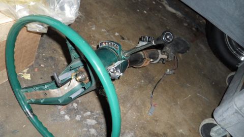 1972 Ford Ranchero - A green steering wheel and column assembly with a PRNDL indicator and disconnected wires lies on a concrete floor.