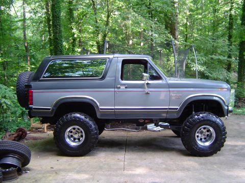 1986 Ford Bronco - This lifted Ford Bronco is parked in a wooded area with a trampoline in the background.