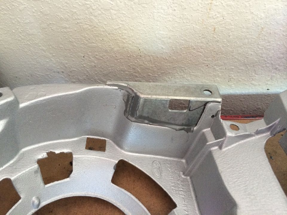 Silver-painted cast metal automotive bracket with sheet-metal tab close-up