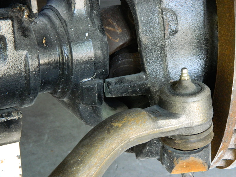 Close-up of a vehicle's front axle and steering linkage with Supermotors.net logo