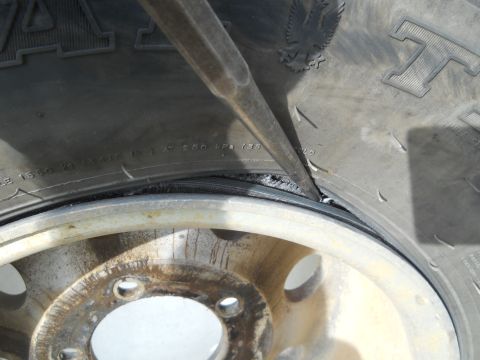 1992 Ford Bronco - A tool is used to pry the tire bead away from a rusty wheel rim, revealing tire sidewall markings.