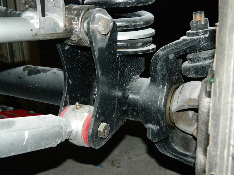 close-up of vehicle suspension components, including a coil spring and linkage with red bushings